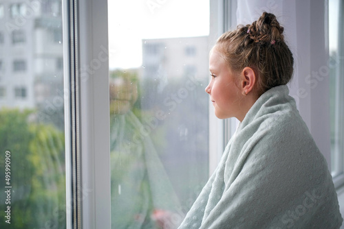 The girl looks out the window at the rain. The child is sad near the window because of the bad weather. Free Download The girl looks out the window at the rain. The child is sad near the window because of the bad weather. - GFXLoad