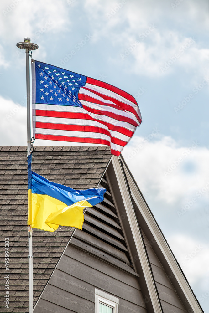 Ukrainian flag flying beneath American flag on windy day at residential home - Close-up