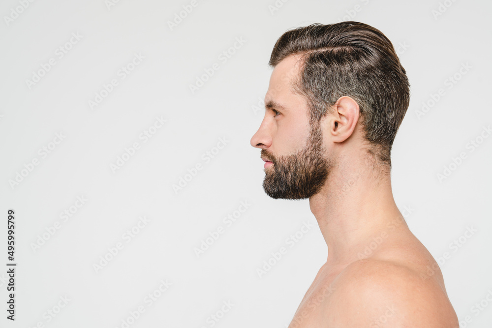 Obraz premium Side view portrait of caucasian naked young shirtless man with beard isolated in white background. Body care skin care male beauty concept