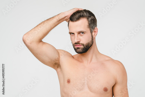Caucasian young shirtless naked man with strong muscles looking at camera touching his hair taking care of his body and skin isolated in white background