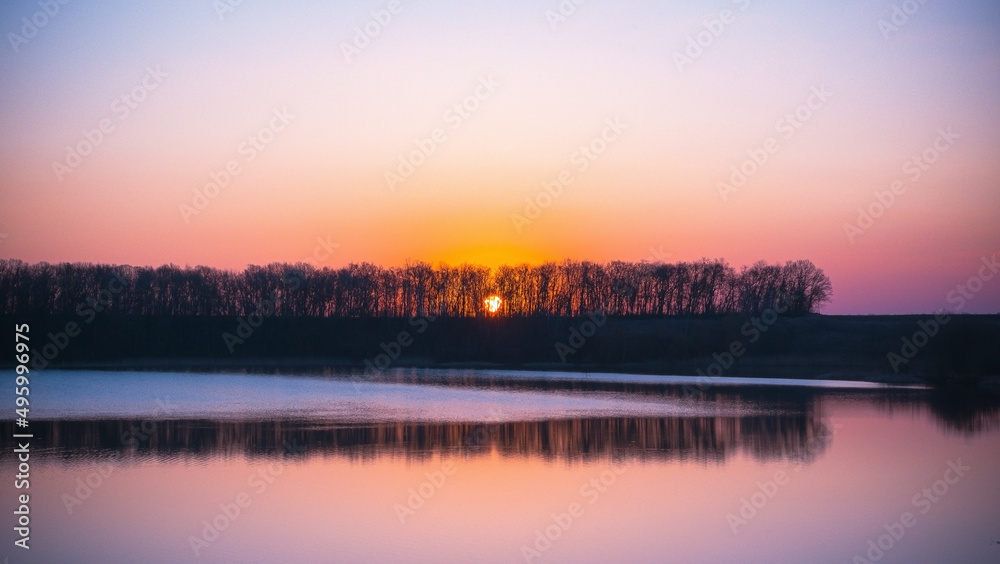 Panoramic view of the spring landscape of the Ukrainian lake at sunrise. The sun shines over the blue lake at dawn. Nature on a sunny morning. Forest on the lake 