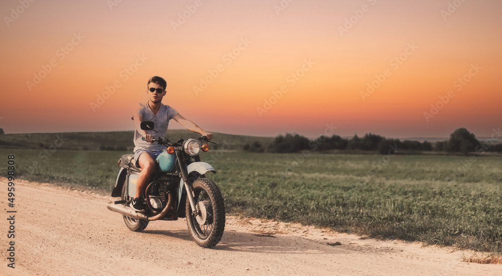 male biker rides on a retro custom motorcycle along a country road at sunset.