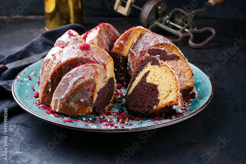 Traditional exotically bundt marble cocoa chocolate cake with icing sugar glaze and freeze dry raspberry topping served as close-up on a Nordic design plate