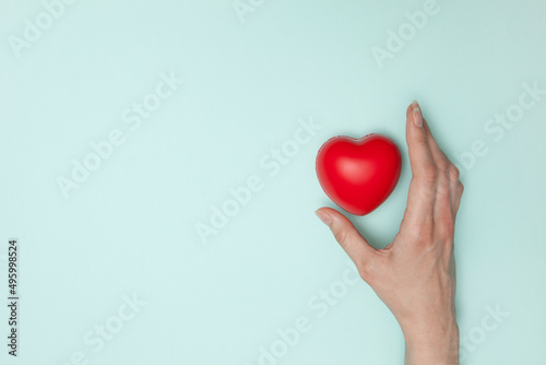 Health, medicine and charity concept - close up of female hands with small red heart