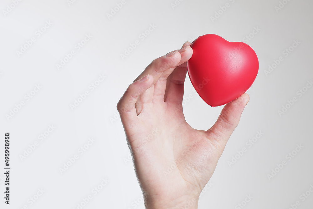 Concept or conceptual red heart sign or symbol held in hands by man or isolated over a white background as a metaphor for love, holiday, wedding, care, valentine, protection or romantic