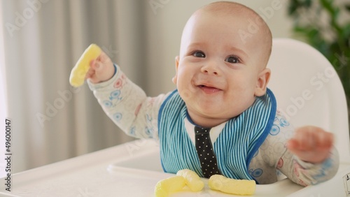 mom Mother feed young baby in white feeding up high chair, first supplement vegetable puree Happy smiling kid eat for the frst time, child with dirty face, little infant boy eating porridge nutrition photo