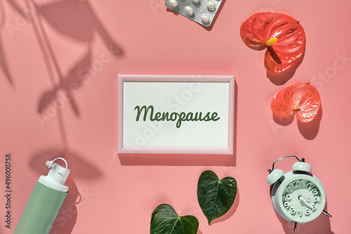 Menopause, text in pink frame. HRT Replacement hormone therapy concept. Pink background with exotic leaves, flowers, pills, estrogene gel. Sunlight, long floral shadows. photo