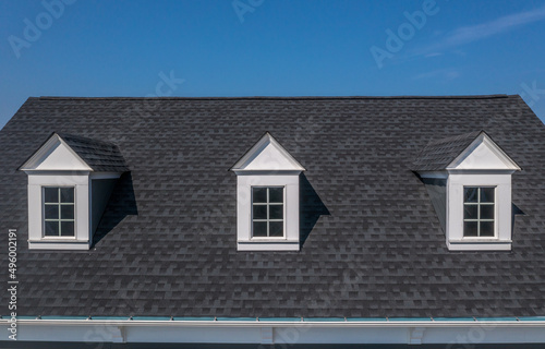 Closeup view of three white dormer windows on a classic roof with blue sky background