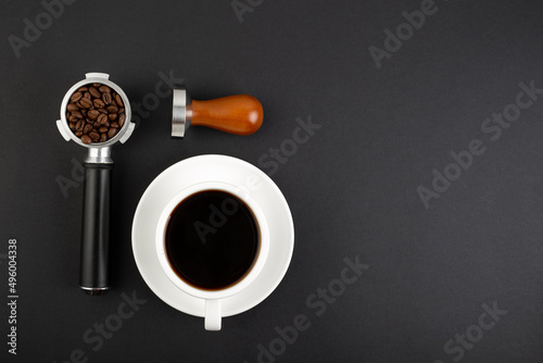 Barista Kit. Coffee Tamper Brown Wooden Handle, coffee horn with beans and white cup espresso, flatlay on black background. Barman tool for pressing down ground coffee, a tamper for a coffee machine