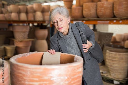 Gray haired woman selecting decorative earthenware pot in home goods store.