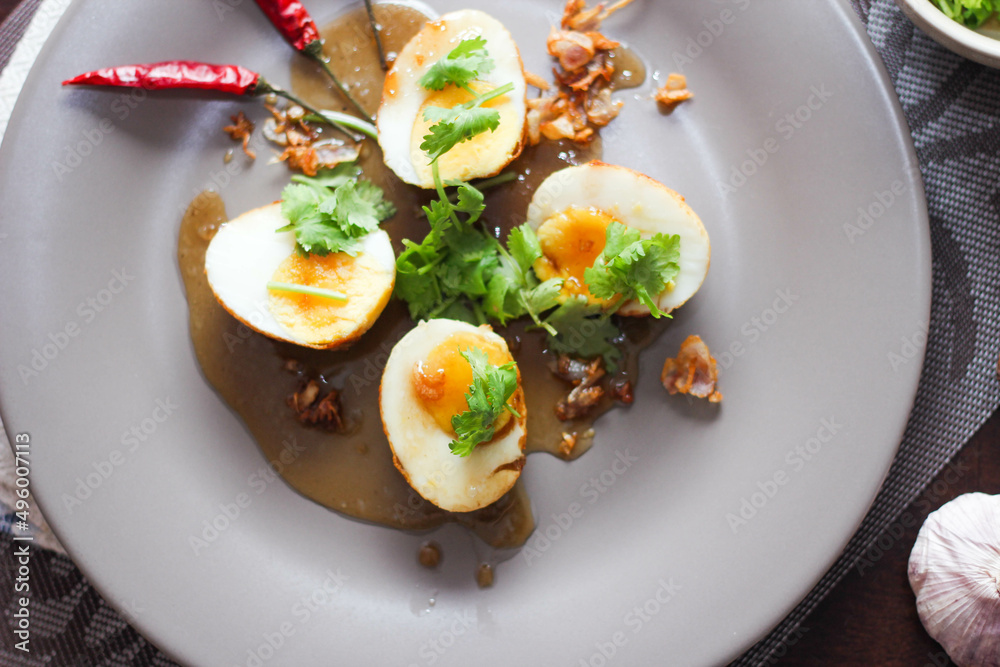 Egg with Tamarind Sauce in a white plate served on a wooden table with coriander sprinkles, is a popular local dish that Thai people eat. Egg with Tamarind Sauce in a white plate served on a wooden table with coriander sprinkles, is a popular local dish that Thai people eat.