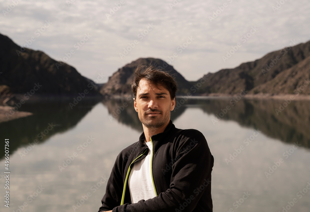 Vacations. Portrait of a handsome man with the lake and mountains in the background. Beautiful environment and sky reflection in the water surface. 