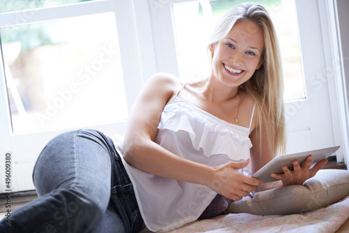 This tablet is the best thing I couldve bought. Smiling young woman lying on the floor while using her tablet - portrait.