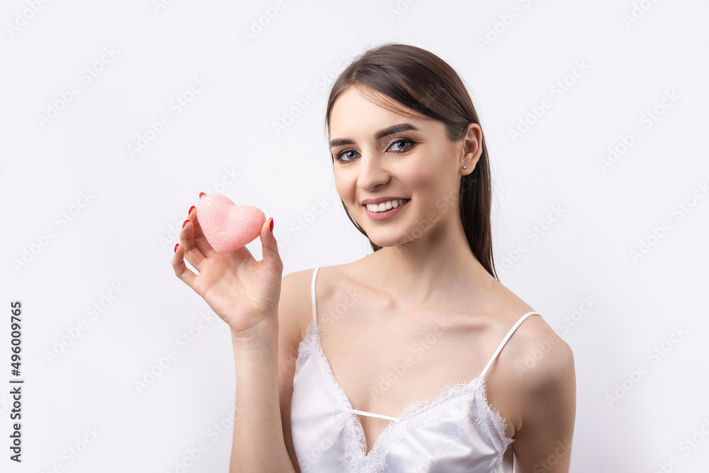 Beautiful smiling woman with clean skin, natural make-up and white teeth on a gray background. Holding a pink hygienic heart.