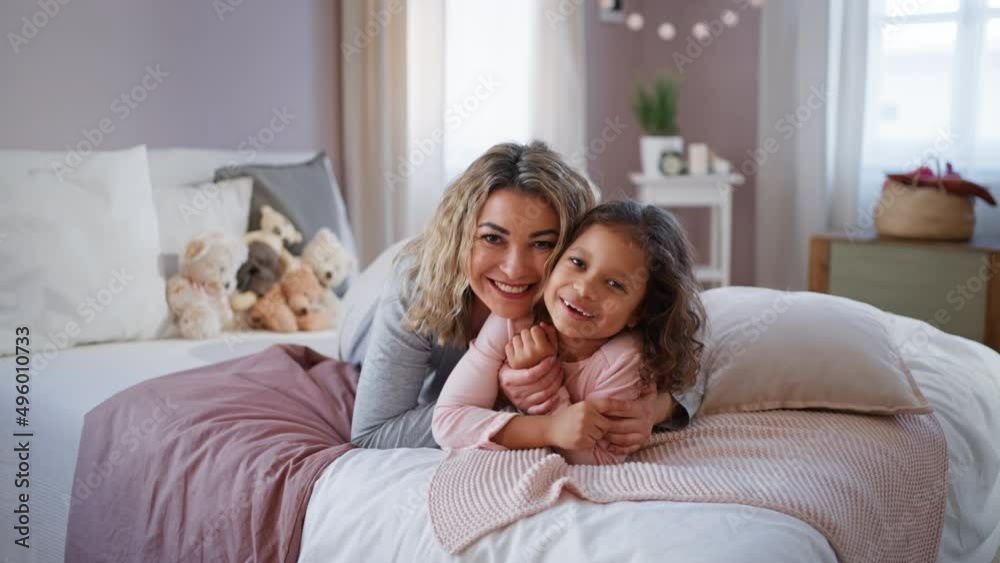 Happy mother with her little daughter lying on bed and looking at camera at home.