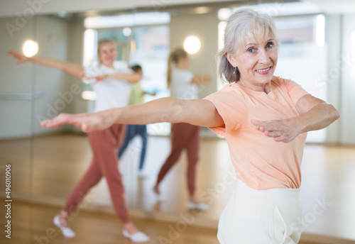 Portrait of elderly smiling european woman and people dancing in modern studio