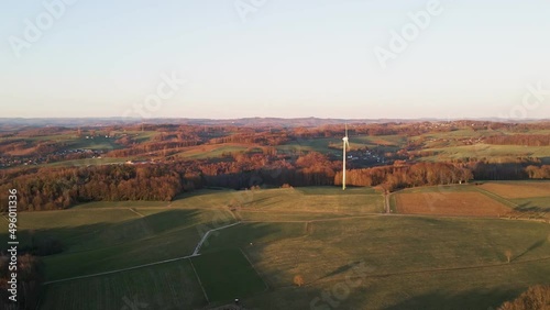 Colourful sunset illuminating partially logged forests and green fields with one wind turbine in western Germany. Aerial dolly zoom effect photo