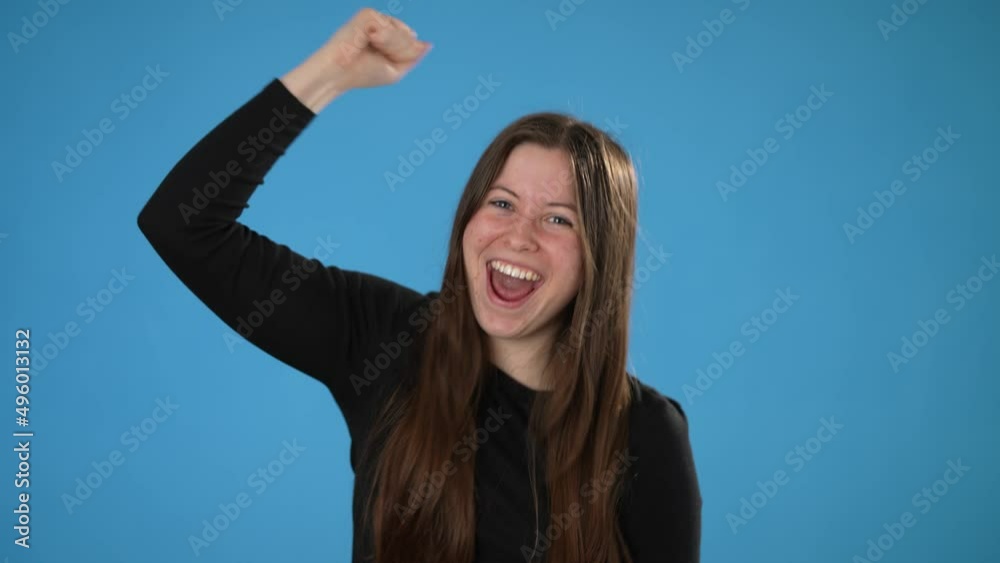 Portrait of happy young brunette woman 20s wear black shirt look camera surprised ask what wow omg no way do winner gesture say yes put hands up isolated on plain blue background in studio Portrait of happy young brunette woman 20s wear black shirt look camera surprised ask what wow omg no way do winner gesture say yes put hands up isolated on plain blue background in studio