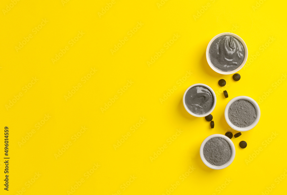 Bowls of activated carbon facial mask, powder and pills on yellow background Bowls of activated carbon facial mask, powder and pills on yellow background
