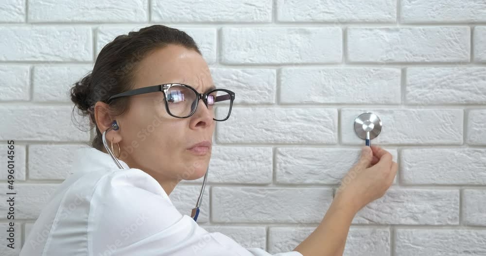 Doctor with stethoscope in ears. A view of a smart doctor with a stethoscope in her ears listen the wall in the room. Doctor with stethoscope in ears. A view of a smart doctor with a stethoscope in her ears listen the wall in the room.