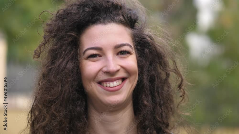 Portrait of curly smiling woman looking at camera. Happy girl standing in the park. Happy beautiful woman smiling at camera. Portrait of curly smiling woman looking at camera. Happy girl standing in the park. Happy beautiful woman smiling at camera.