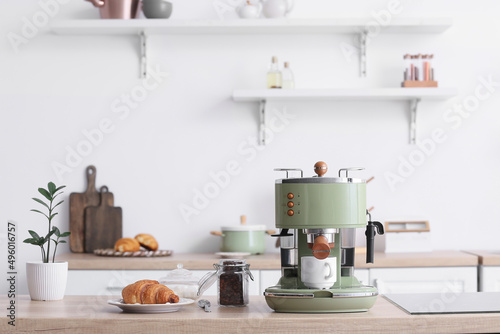 Modern coffee machine, jar of beans and croissant on counter in kitchen