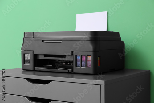 Printer with paper on chest of drawers near green wall, closeup