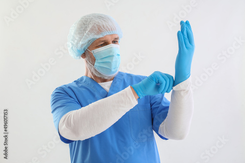 Mature male doctor in medical mask and gloves on white background