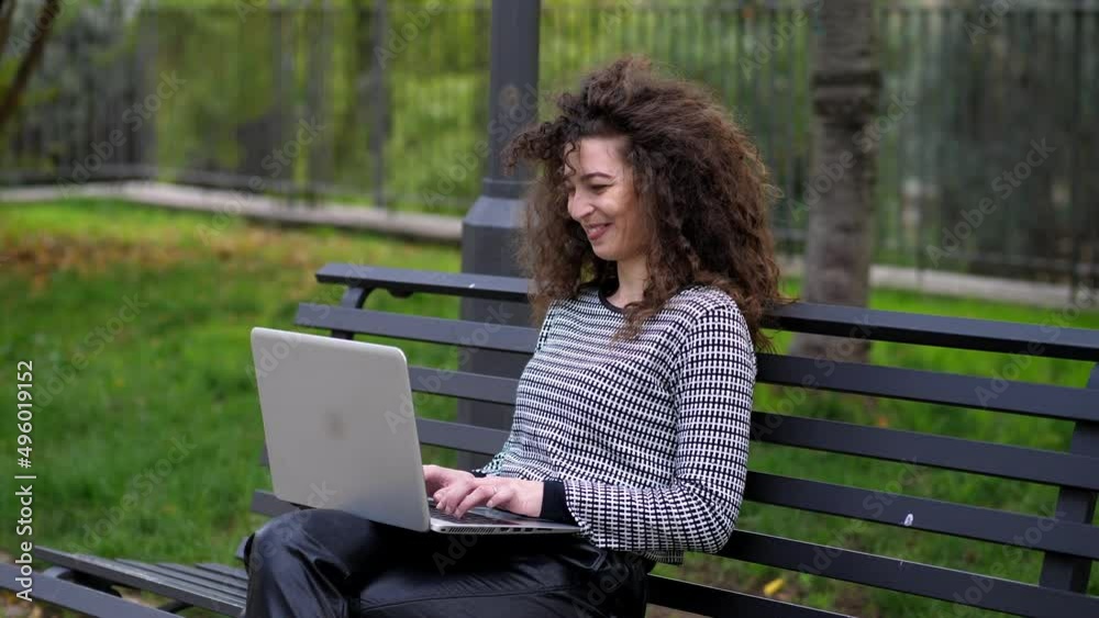 Happy young beautiful curly student girl sitting in the park using laptop Happy young beautiful curly student girl sitting in the park using laptop