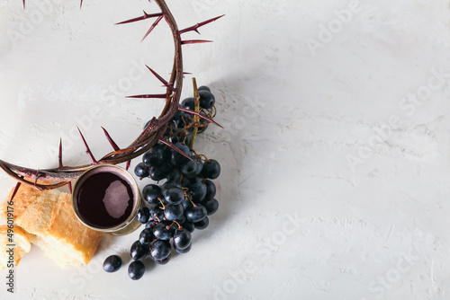 Cup of wine with grapes, bread and crown of thorns on light background photo