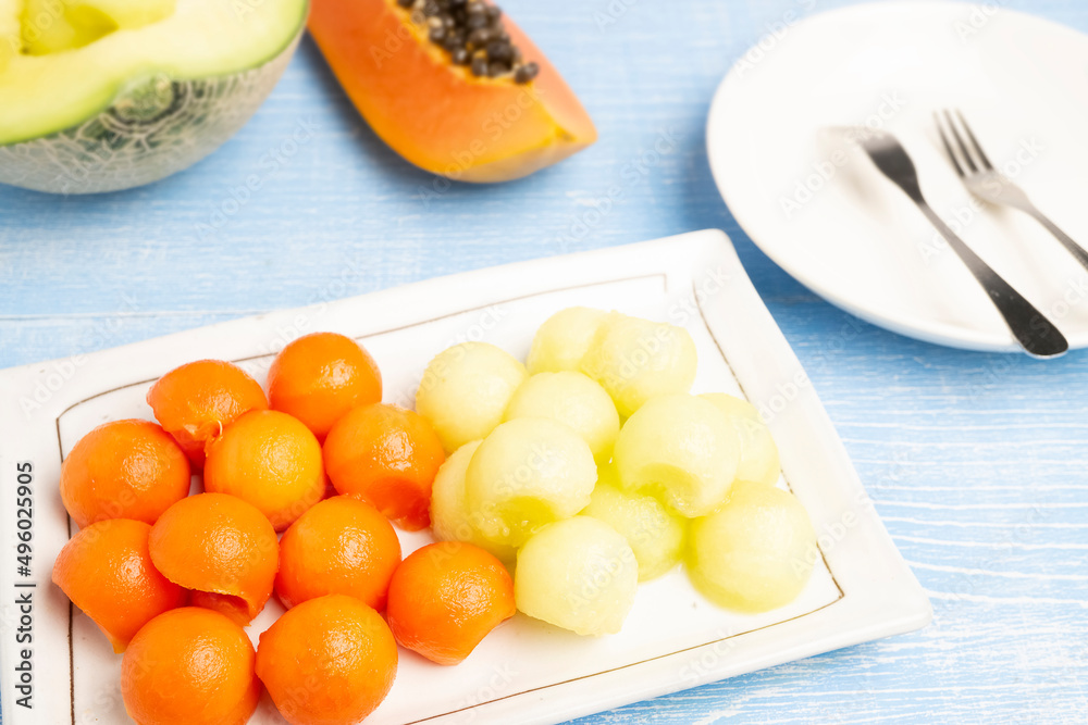 Organic Fresh Ripe Papaya, Thai tropical fruit and Fresh Japanese Melon cut in circle shapes serving on a white plate with blurred background of both types of fruits cut in pieces.	
