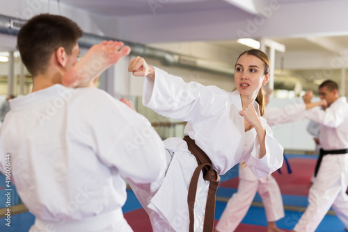 Young woman fighting with her sparring-partner during group karate training in gym.