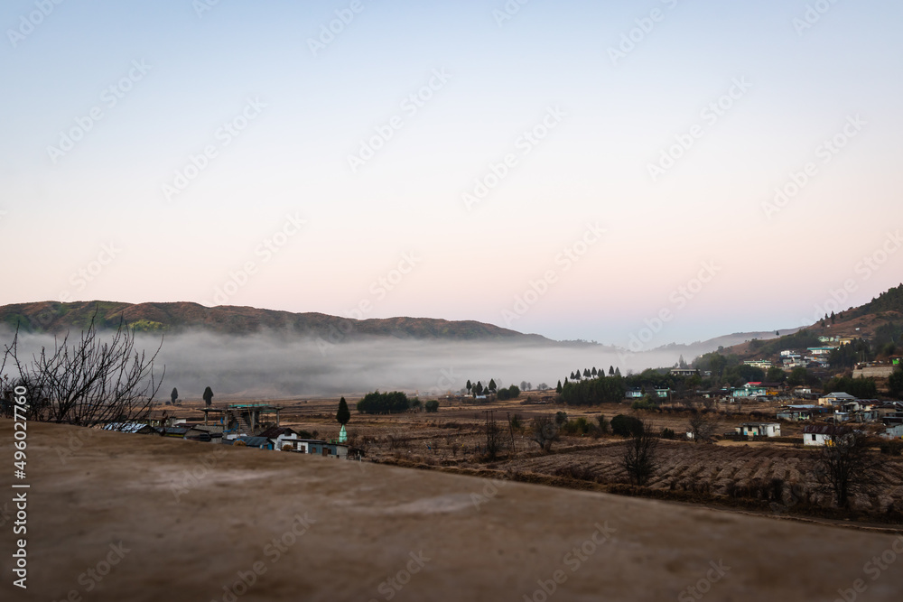 small village at the mountain foothills covered with white mist ans dramatic sky at sunrise