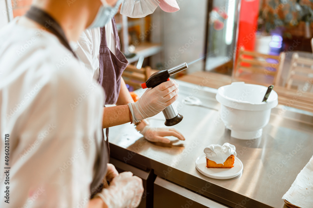 Confectioner with gas burner and colleague in mask work with sponge cake in bakery Confectioner with gas burner and colleague in mask work with sponge cake in bakery
