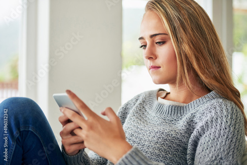 Sending some texts to her friends. Cropped shot of an attractive young woman sending a text message while chilling at home.