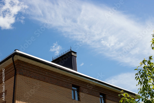A roof with a chimney on the background of a blue summer sky. © Sofya