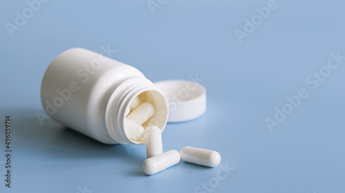 White capsules scattered from white plastic medicine container