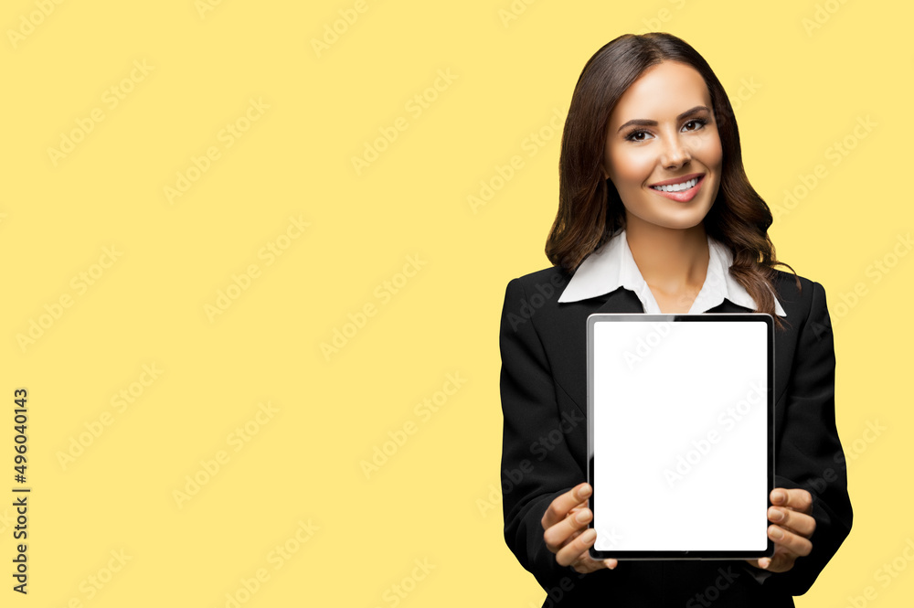 Portrait of happy smiling brunette businesswoman showing tablet pc, touchpad, with copy space area for text, isolate over yellow color background. Confident attractive business woman at studio Portrait of happy smiling brunette businesswoman showing tablet pc, touchpad, with copy space area for text, isolate over yellow color background. Confident attractive business woman at studio