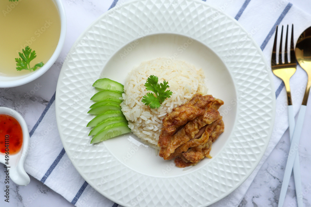 Hainanese fried chicken over oily rice with chili sauce in white plate - Famous Singaporean food and in Thai called Khao Mun Gai Tord at top view Hainanese fried chicken over oily rice with chili sauce in white plate - Famous Singaporean food and in Thai called Khao Mun Gai Tord at top view