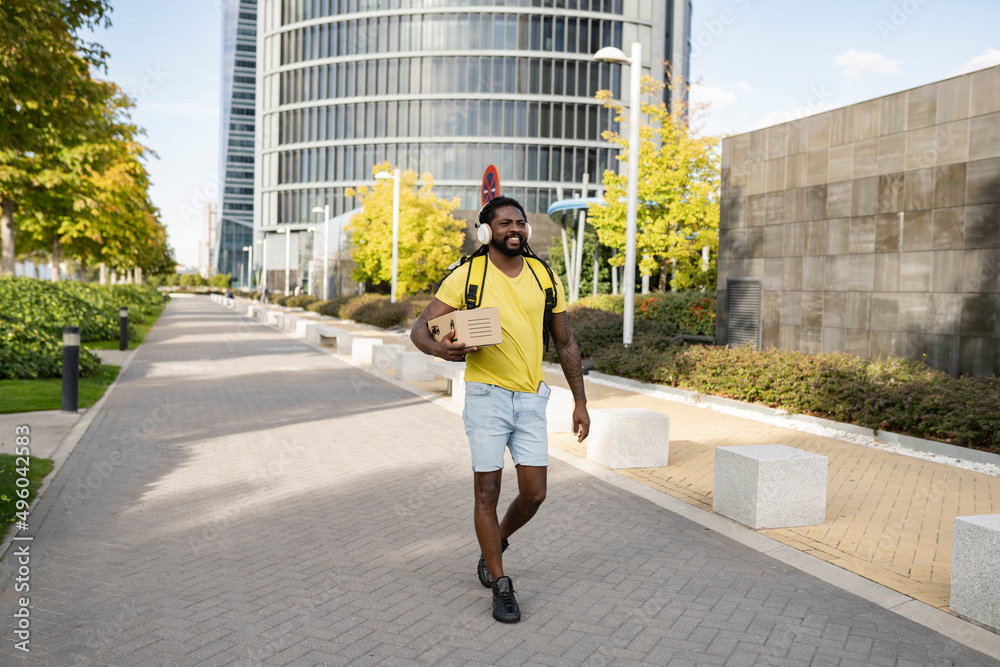 Young African American male delivery man carrying a package and while walking along a city footpath. Young African American male delivery man carrying a package and while walking along a city footpath.