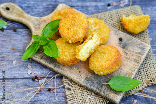 Vegetarian Cheese oven baked Croquette with fresh basil on Wooden background. Yellow cheese nuggets