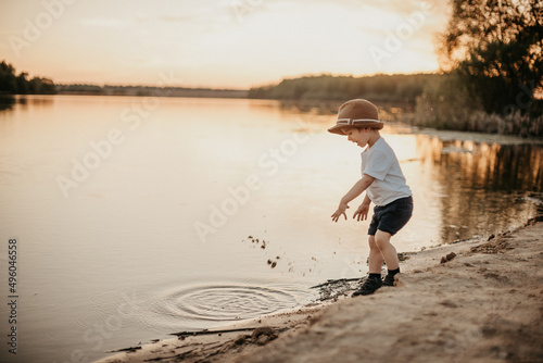 A little boy in a hat throws hay and laughs in the summer on a sunny day