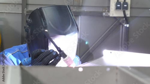 A welder in protective clothing and a mask works with a welding machine
