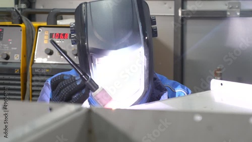 A welder in protective clothing and a mask works with a welding machine