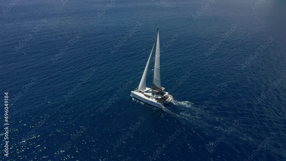 Aerial footage, rear view of luxury sailboat sailing on a deep blue sea with white wakes. Camera follow catamaran in blue ocean water