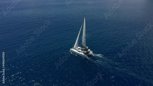 Aerial footage, rear view of luxury sailboat sailing on a deep blue sea with white wakes. Camera follow catamaran in blue ocean water photo