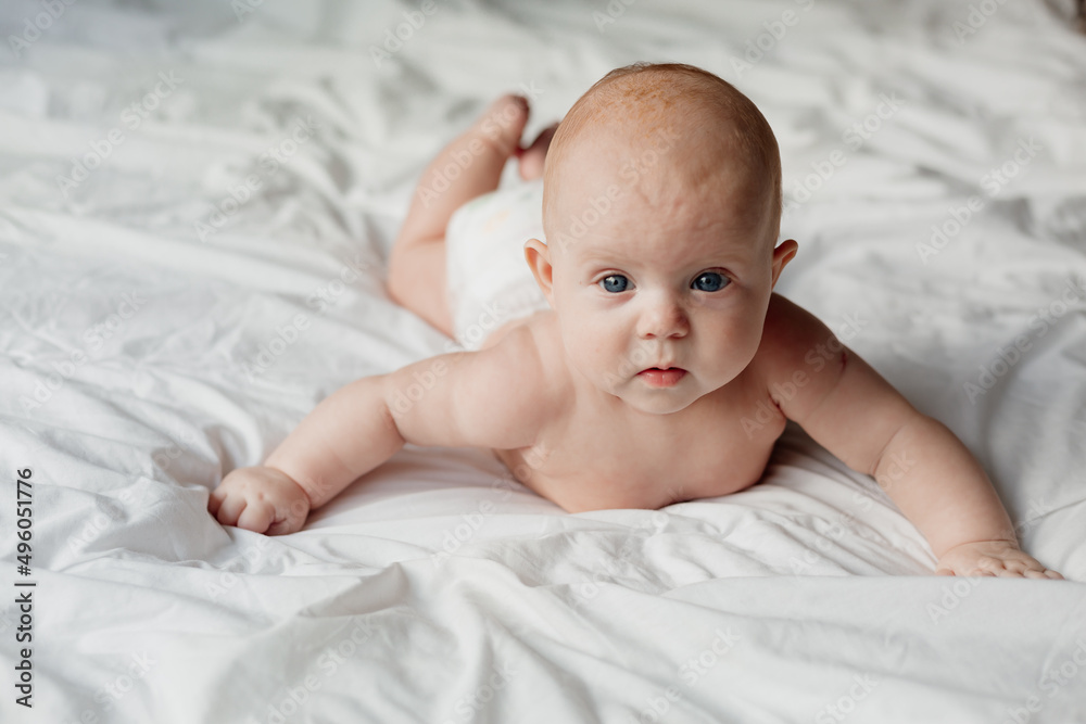 cheerful smiling newborn baby in a diaper lies on his stomach on a white bed cheerful smiling newborn baby in a diaper lies on his stomach on a white bed