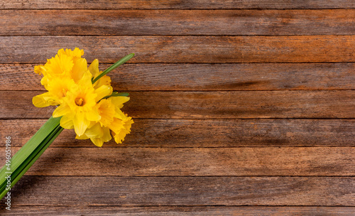 a bouquet of yellow narcissus flowers on a brown wooden background with copy space