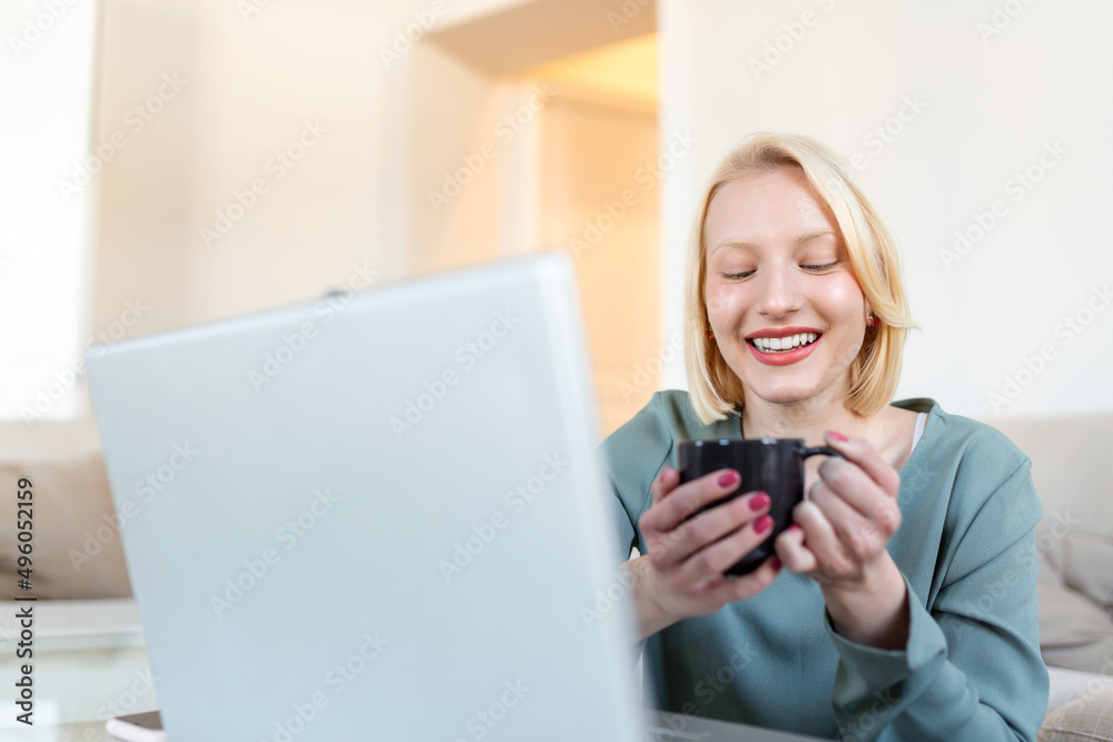 Positive young woman freelancer watching video in blog on netbook and having a coffee at comfortable home. Beautiful young business woman working on laptop.Freelancer connecting to internet Positive young woman freelancer watching video in blog on netbook and having a coffee at comfortable home. Beautiful young business woman working on laptop.Freelancer connecting to internet