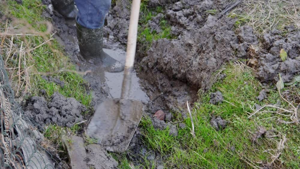 A man in rubber boots clears a channel for water flow with a shovel. A man in rubber boots clears a channel for water flow with a shovel.